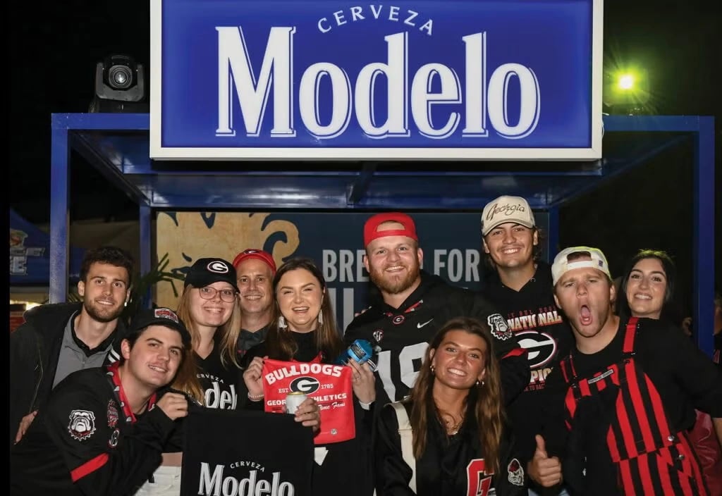 College football fans posing at Cerveza Modelo signage during Cogent World's Full-Time Fans activation