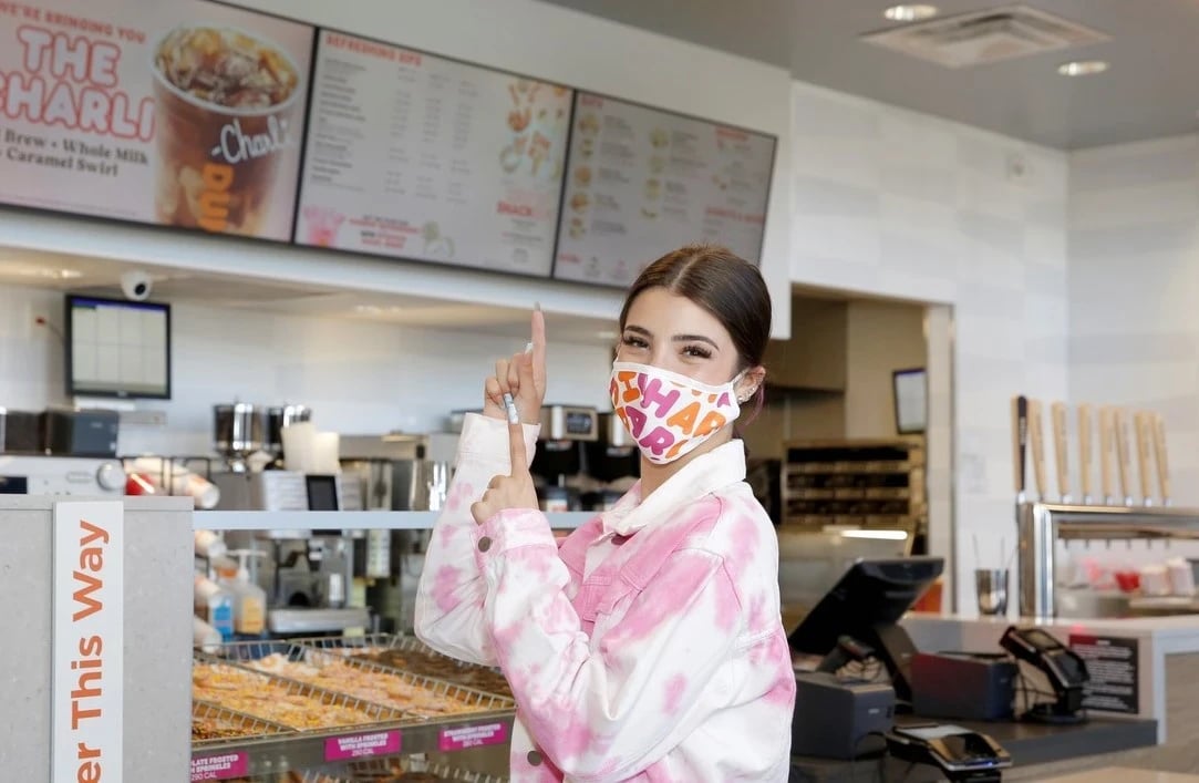 Charli D'Amelio pointing at the Dunkin menu board announcing The Charli cold brew