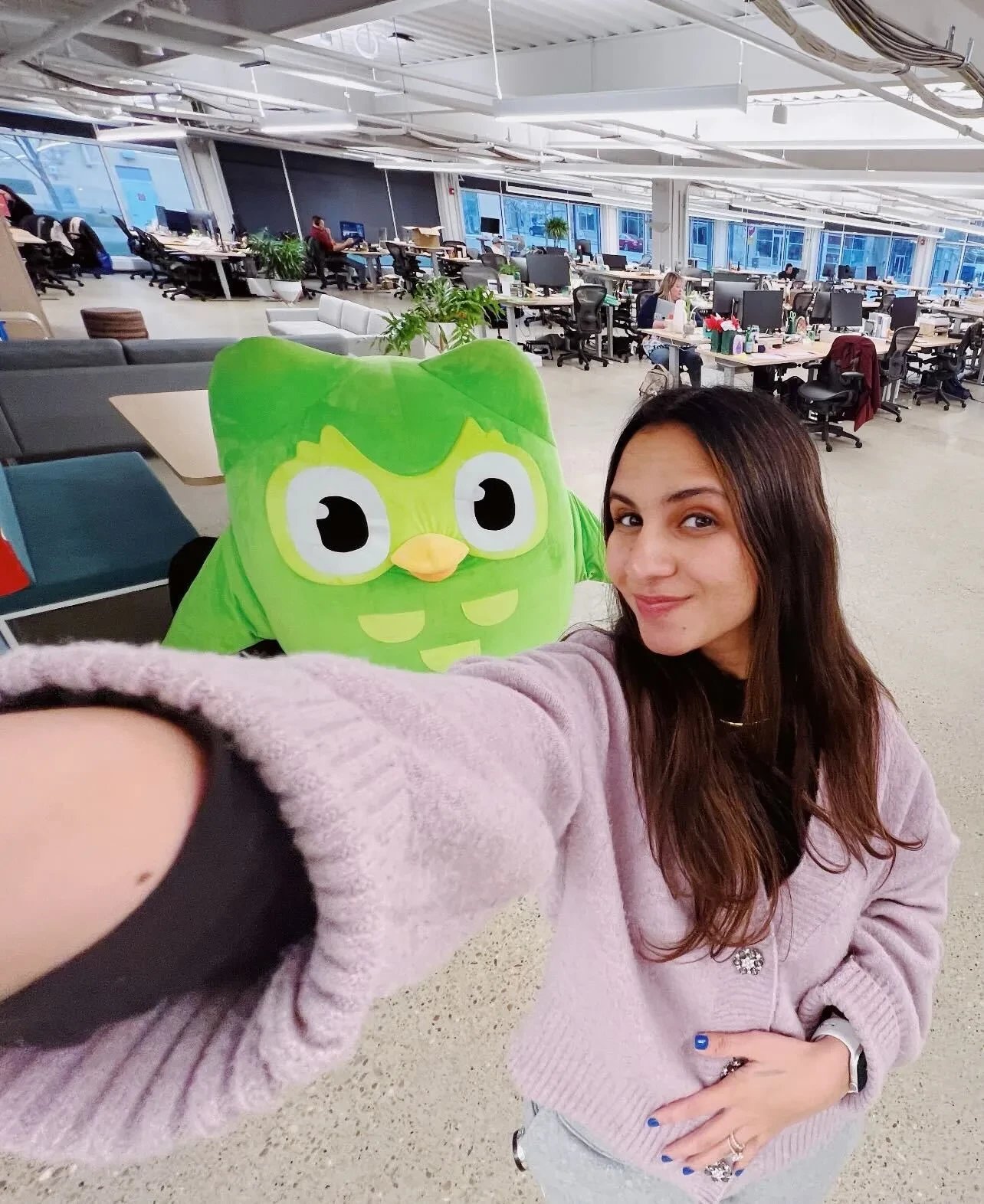 Duolingo's social lead taking a selfie with the Duo owl mascot in the company's open-plan office